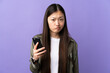 © luismolinero - Young Chinese girl using mobile phone over isolated purple background with sad expression