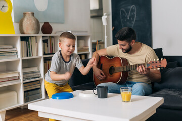 Canvas Print - father and son having great time together at home. playing guitar and singing