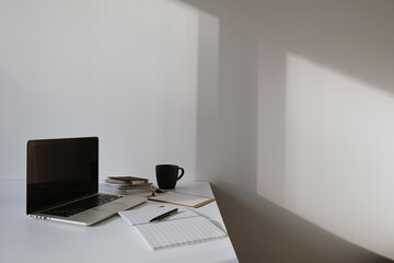 Wall Mural - Laptop on table with coffee cup, paper sheet against white wall. Minimalist home office workspace.