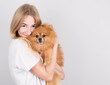 © Studio Nova - A beautiful blonde young woman hugs and kisses her spitz puppy. Love between dog and owner. Isolated on a gray background.
