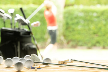 Wall Mural - Golf balls, golf equipment and golf club on table on driving range with golfer in background