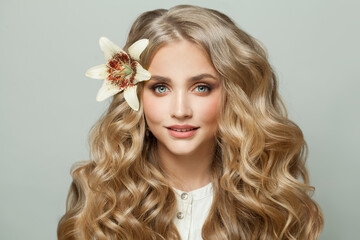 Wall Mural - sweet cheerful woman with flower in curly blonde hair on white background