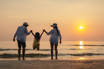 Wall Mural - Happy asian family jumping together on the beach in holiday. Silhouette of the family holding hands enjoying the sunset on the  beach.Happy family and vacations concept.