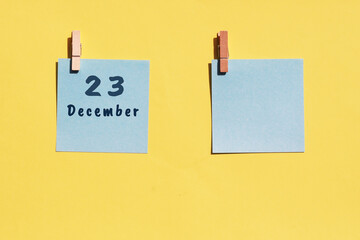 23 December. 23th day of the month, calendar date. Two blue sheets for writing on a yellow background. Top view, copy space. Winter month, day of the year concept