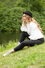 Wall Mural - blonde woman in black hat sitting by the river