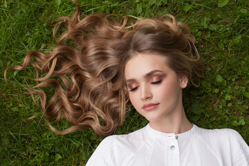 carefree young woman with curly blonde hair lying on green grass outdoor