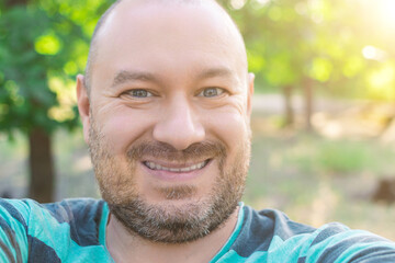 Contented plump unshaven middle-aged man smiling outdoors.