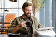 © Drobot Dean - Unshaven smiling man drinking coffee while reading newspaper in cafe