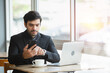 © eakgrungenerd - Businessman wear black suit using smartphone working laptop sitting in coffee shop. handsome male business worker in relax time.