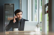 © eakgrungenerd - Businessman wear black suit talking telephone working laptop sitting in coffee shop. handsome male business worker in relax time.