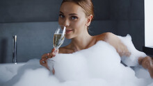 Young Woman Taking Bath With Foam And Drinking Champagne In White Bathtub