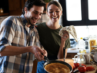 Boyfriend and girlfriend making pancakes at home. Young couple having fun in the kitchen