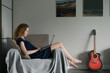 © Demetr White/Stocksy - girl sits on a sofa and works behind a laptop on a background of a wall with a photo and a guitar