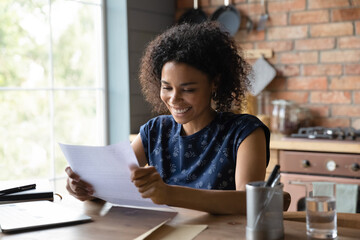 Joyful young mixed race female open paper written letter happy to read positive news from friend. Satisfied self employed black businesswoman get official answer about receiving credit loan from bank