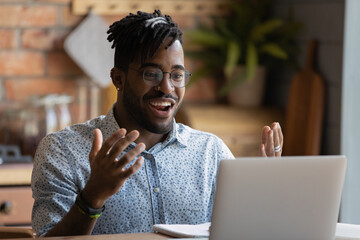Happy young afro american man software developer run program code on pc enjoy reaching successful result. Overjoyed black guy look on laptop screen splash hands having winning hand at online blackjack
