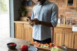 © fizkes - Check web for recipe. Cropped shot of young african male stand by kitchen table use cell search details of preparing dish online. Black man husband cooking food consult with wife using wifi internet