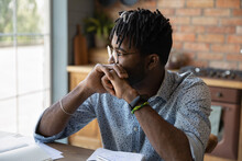 Thinking By Window. Pensive Afro Caribbean Guy Student Hipster Sit At Table Leaning On Folded Hands Reflect On Training Task. Concentrated Young Black Man Freelancer Creating Idea Planning Future Work
