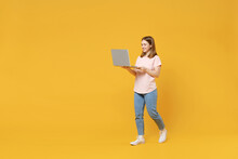 Full Length Of Young Caucasian Student Woman 20s In Basic Pastel Pink T-shirt, Jeans Holding Laptop Pc Computer Chatting Surfing Internet Walk Go Isolated On Yellow Color Background Studio Portrait.