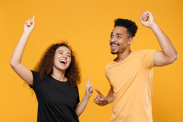 Young couple two happy friends family african overjoyed excited man woman 20s wearing black t-shirt do winner gesture point index finger up celebrating isolated on yellow background studio portrait.