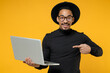 © ViDi Studio - Young freelancer surprised copywriter african man 20s wearing stylish black shirt hat eyeglasses point index finger on laptop pc computer isolated on yellow orange color background studio portrait