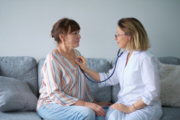 Female professional doctor showing medical test result explaining prescription using digital tablet app visiting senior woman patient at home sitting on sofa. Elderly people healthcare tech concept.