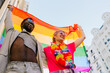 © MyMicrostock/Stocksy - Happy multiracial couple raising LGBT pride flag in street in daylight