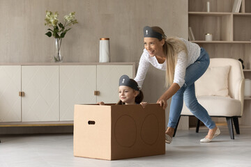 Wall Mural - Smiling young mother ride excited little daughter in imaginary ship play pirate game together at home. Happy caring mom and small girl child engaged in playful activity on leisure family weekend.