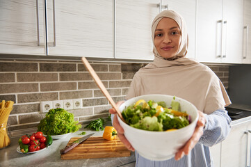 Arab Muslim woman holds a bowl with salad and shows it to the camera