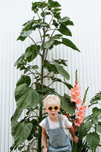 Toddler With Sunglasses In Front Of Flower Garden With Sunflowers And Gladiolus