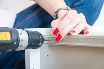 Self assembling furniture at home by woman using electric screwdriver.