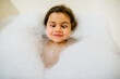 © Jessica Klaus/Stocksy - Young girl making silly face laying in a bubble bath.