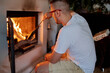 © Tatiana Timofeeva/Stocksy - autumn mood man has lit a fireplace at home and is warming himself and looking at the fire