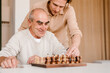 © Alina Hvostikova/Stocksy - Happy senior man with son playing chess at home