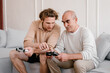 © Alina Hvostikova/Stocksy - Young man teaching senior father to play video game