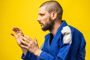 Portrait of adult man in blue gi kimono standing in front of yellow background with copy space side view in guard fighting stance