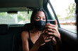 © Jimena Roquero/Stocksy - Young attractive woman with protective mask inside a car looking at her smart phone.