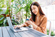 © twinsterphoto - Beautiful young Asian woman smiling and holding bank credit card for payment on laptop for online shopping sitting in modern cafe