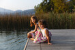 © Michela Ravasio/Stocksy - Little sisters sitting by the lake together at sunset