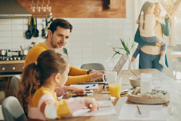 Wall Mural - Smiling father working on laptop and talking to his daughter at home.