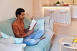 © Ivan Gener/Stocksy - Young man reading on his sofa