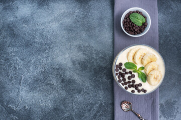 Wall Mural - Healthy breakfast, dessert with milk yogurt banana and chocolate on a plate. Dark concrete background. Top view, copy space.