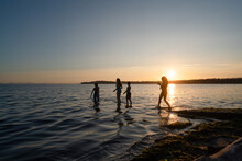 Wide View Silhouette Of Children Wading Into Water At Sunset