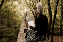 Young Woman Sitting In Old Pipeline Drawing In Notebook In Forest During Autumn