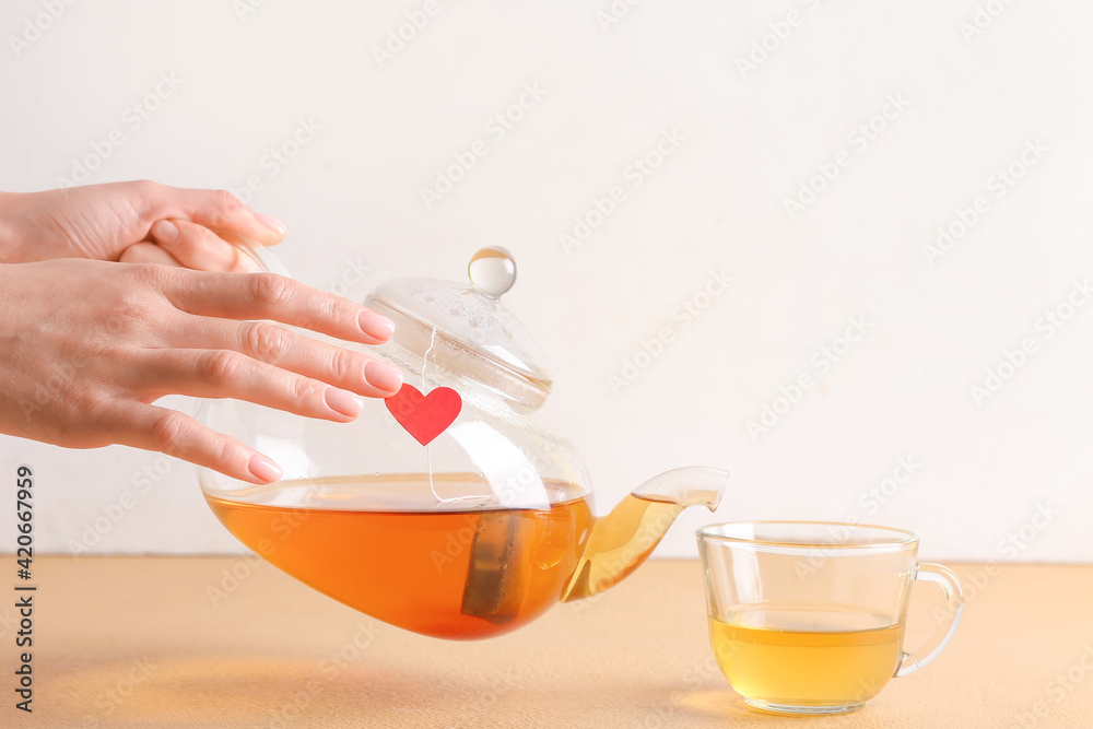 Woman pouring aromatic black tea from teapot into cup on color background