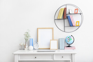 Stylish workplace with laptop and bookshelf against light wall in room