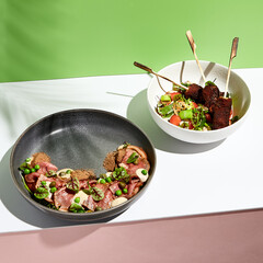 Wall Mural - Roast beef salad with green peas and Avocado salad. Salad bowl on white table with green and pink wall. Sunlight with harsh shadow of green tropic leaf.