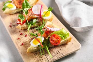 Smoked Salmon Bruschetta with Pita Bread, Quail Egg and Vegetables. Canape fish food appetizer on grey table with wooden board. Healthy, gourmet, appetizers food concept.