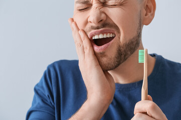 Wall Mural - Man with aching teeth and brush on grey background