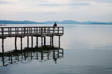 Man Relaxing On A Pier Looking Out At A Calm Lake.