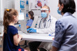 © DC Studio - Caring doctor discussing symptoms with mother in medical clinic. Specialist in pediatry medicine with protection mask and visor against covid19 talking about diagnostic and healtcare treatment
